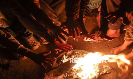 Anak-anak berkumpul di sekitar api unggun untuk menghangatkan diri di kamp pengungsi Palestina di tepi pantai di Deir al-Balah, Jalur Gaza tengah, Jumat (27/12/2024). Anak-anak Gaza yang tinggal di dalam tenda pengungsian hidup dengan penuh keterbatasan. Mereka harus menghadapi ancaman hawa dingin dan keterbatasan pasokan makanan. Tenda-tenda yang dibangun seadanya tidak melindungi mereka sepenuhnya dari hawa dingin. Agresi Israel ke Palestina telah membuat 90 persen warga Gaza mengungsi dan tinggal di kamp pengungsian.