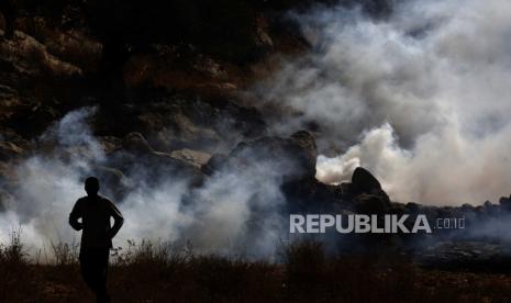 Palestina Kecam Pembangunan Rumah Israel di Tepi Barat. Warga Palestina mencari perlindungan dari gas air mata yang ditembakkan oleh tentara Israel selama demonstrasi menentang permukiman Israel di desa Bet Dajan dekat kota Nablus, Tepi Barat utara,  Jumat (9/10/2020). 