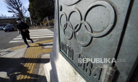  Seorang pria yang mengenakan masker untuk membantu melindungi dirinya dari virus korona berlari di dekat plak untuk menghormati Olimpiade Tokyo 1964 Senin, Januari. 25, 2021 di Tokyo. 