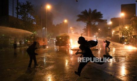  Demonstran mencalonkan diri sebagai polisi menggunakan meriam air untuk membubarkan mereka pada peringatan satu tahun dimulainya protes massa anti-pemerintah atas ketidaksetaraan di Santiago, Chili, Minggu, 18 Oktober 2020. 