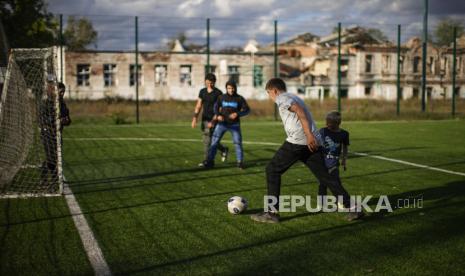 Anak laki-laki bermain sepak bola di samping sekolah yang hancur, di latar belakang, di Izium, Ukraina, Senin, 3 Oktober 2022. Komisioner Rusia untuk hak anak-anak pada Selasa (3/4/2023) menolak tuduhan Pengadilan Kriminal Internasional (ICC) bahwa negara ini, bertanggung jawab telah mendeportasi anak-anak dari Ukraina secara paksa dan tidak sah, sebagai tuduhan palsu.