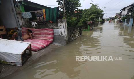 Warga duduk di samping jalan yang tergenang banjir di Dusun Nyanyat, Benjeng, Kabupaten Gresik, Jawa Timur, Senin (14/12/2020). Banjir itu akibat luapan Kali Lamong di Kabupaten Gresik, Jawa Timur. 