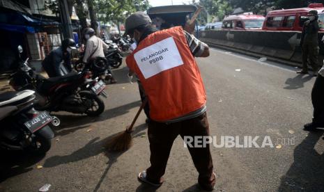 Warga dengan menggunakan rompi diberikan sanksi menyapu sampah akibat melanggar Pembatasan Sosial Berskala Besar (PSBB) karena tidak menggunakan masker di tempat umum di Kawasan Pasar Minggu, Jakarta, Rabu (13/5). Sanksi bagi pelanggar PSSB ini mulai diberlakukan, adapun pengenaan sanksi kepada pelanggar mulai dari sanksi sosial hingga denda