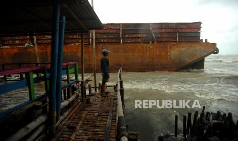 Seorang warga memperhatikan kapal Tongkang  yang terdampar di pantai (ilustrasi)