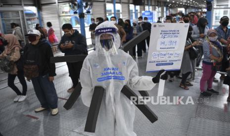 Anggota komunitas pecinta Transjakarta mengenakan baju hazmat dengan membawa poster berisi informasi jumlah kasus positif di Jakarta saat melakukan sosialisasi protokol kesehatan di Halte Transjakarta Harmoni, Jakarta, Rabu (15/7/2020). Sosialisasi tersebut untuk mengingatkan penumpang Transjakarta agar selalu menaati protokol kesehatan saat menggunakan transportasi publik guna mengantisipasi penyebaran COVID-19. 