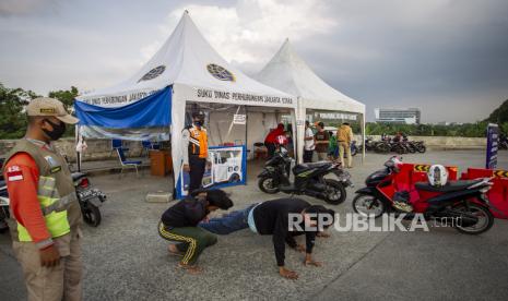 Petugas memberikan hukuman kepada warga yang tidak mengenakan masker saat melintasi check point pelaksanaan Pembatasan Sosial Berskala Besar (PSBB) di Jl. Inspeksi Banjir Kanal Timur, Rorotan, Jakarta Utara, Jumat (29/5/2020)