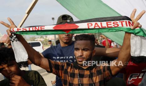 Seorang pengunjuk rasa menunjukkan tanda v sementara yang lain mengibarkan bendera nasional mereka di dekat pagar perbatasan Jalur Gaza dengan Israel, selama protes menandai peringatan serangan pembakaran tahun 1969 di masjid Al-Aqsa Yerusalem oleh seorang turis Australia yang kemudian ditemukan sakit jiwa, timur Kota Gaza, Sabtu, 21 Agustus 2021. Pengadilan Israel Bekukan Pembongkaran Masjid di Yerusalem