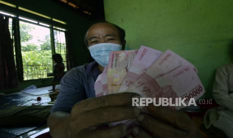 Warga menunjukkan uang tunai saat penyaluran bantuan sosial tunai (BST).