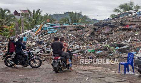 Orang-orang melihat reruntuhan bangunan yang rata saat gempa di Mamuju, Sulawesi Barat, Indonesia, Sabtu, 16 Januari 2021. Jalan dan jembatan yang rusak, pemadaman listrik dan kurangnya alat berat pada hari Sabtu menghambat penyelamat Indonesia setelah kuat dan dangkal gempa bumi mengakibatkan sejumlah orang tewas dan luka-luka di pulau Sulawesi.