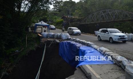 Kendaraan melintasi badan jalan nasional yang amblas di kelok hantu Aia Angek, Tanah Datar, Sumatera Barat, Ahad (21/4/2024). Jalan Raya Padang-Bukittinggi yang terdampak banjir lahar dingin Gunung Marapi dua pekan lalu itu kini amblas sehingga arus lalu-lintas dilakukan sistem buka tutup.  