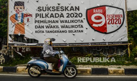 Pengendara motor melintas di dekat spanduk sosialisasi Pemilihan Kepala Daerah (Pilkada) yang terpasang di kawasan Ciputat, Tangerang Selatan, Banten, Senin (28/9). Meskipun banyak desakan dari sejumlah organisasi dan kalangan masyarakat untuk menunda Pilkada karena dikhawatirkan dapat menjadi klaster penularan Covid-19, Pilkada serentak yang diadakan di 270 daerah di Indonesia itu akan tetap dilaksanakanan pada 9 Desember 2020 dengan menerapkan protokol kesehatan. Republika/Putra M. Akbar