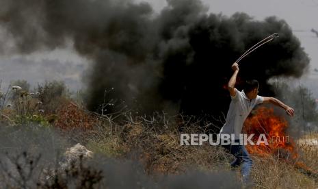 Seorang pengunjuk rasa Palestina menggunakan ketapel untuk melempar batu selama bentrokan dengan pasukan Israel setelah protes terhadap pemukiman Israel di Desa Beta dekat Kota Nablus, Tepi Barat, 28 Mei 2021.