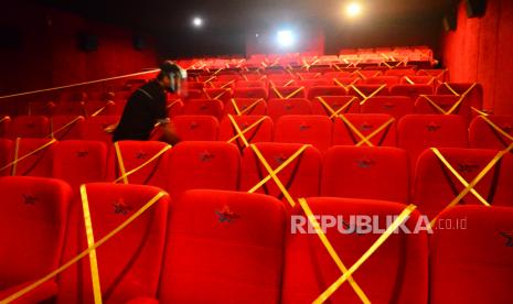 Petugas memasang pita jaga jarak tempat duduk di dalam studio saat pembukaan kembali bioskop. Ilustrasi.