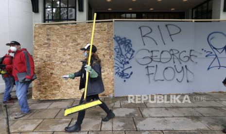 Seorang wanita yang membantu membersihkan pusat kota berjalan dekat grafiti, Minggu, 31 Mei 2020, di Seattle, setelah malam kerusuhan dan protes atas kematian George Floyd, seorang pria kulit hitam yang berada dalam tahanan polisi di Minneapolis. Floyd meninggal setelah ditahan oleh petugas kepolisian Minneapolis pada 25 Mei