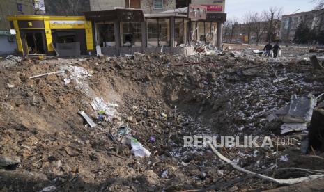 Orang-orang berjalan melewati kawah dari ledakan di Mira Avenue (Avenue of Peace) di Mariupol, Ukraina, Ahad, 13 Maret 2022.