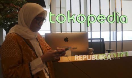 Seorang warga melihat ponselnya dengan latar belakang logo Tokopedia.