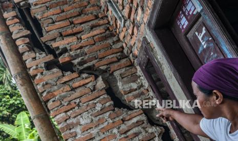 Warga menunjukkan retakan dinding rumah yang rusak akibat pergerakan tanah.