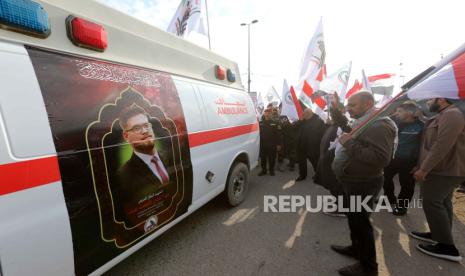   Anggota Pasukan Mobilisasi Populer Syiah (PMF) Irak berkumpul di dekat ambulans yang membawa peti mati rekan mereka, yang terbunuh dalam serangan udara AS baru-baru ini di Irak barat. 