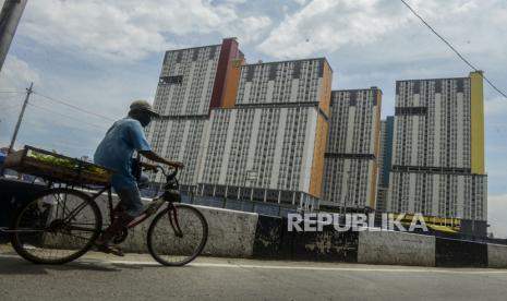 Warga melintas menggunakan sepeda dengan latar belakang Wisma Atlet Kemayoran yang difungsikan sebagai rumah sakit darurat di Jakarta.