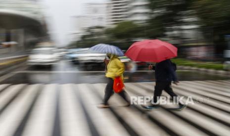 Gambar yang diambil dengan efek kecepatan rana lambat menunjukkan orang-orang yang memegang payung di bawah hujan, melintasi jalan yang sibuk di Jakarta, Indonesia.