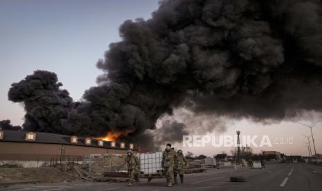 Prajurit Ukraina membawa kontainer dengan latar belakang kobaran api di sebuah gudang setelah pemboman di pinggiran Kyiv, Ukraina, Kamis, 17 Maret 2022. Beberapa rudal Rusia menghantam hanggar perbaikan pesawat di kota Lviv, Ukraina barat pada Jumat (18/3/2022) pagi.