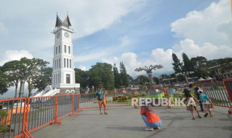 Pengunjung berfoto di pelataran Jam Gadang yang ditutup dengan pagar, di Bukittinggi, Sumatera Barat. Satgas COVID-19 Kota Bukittinggi, Sumatera Barat, memaksa 162 pelanggar protokol kesehatan (prokes) yang terjaring operasi yustisi di daerah ini menjalani tes usap.