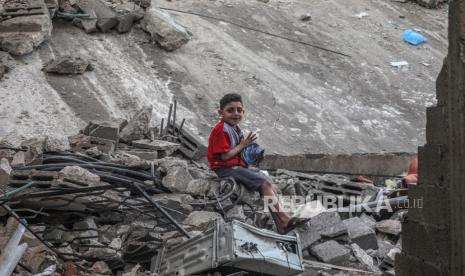 Seorang bocah Palestina duduk di antara puing-puing rumah yang hancur akibat serangan udara Israel di Kota Gaza, Kamis (19/5). (ilustrasi)