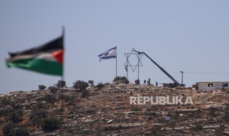 Pemukim Israel menyesuaikan Bintang Daud besar di pos terdepan kucing liar Eviatar yang baru-baru ini didirikan seperti yang terlihat dari desa Palestina terdekat Beita, dekat kota Nablus, Tepi Barat, Jumat, 2 Juli 2021. Israel telah mencapai kompromi dengan pemukim Yahudi yang akan mereka tinggalkan pada akhir minggu dan daerah itu akan menjadi zona militer tertutup, tetapi rumah-rumah dan jalan-jalan akan tetap di tempatnya.