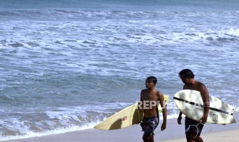 Dua orang warga berjalan dengan membawa papan selancar di Pantai Kuta, Badung, Bali. Mulai 14 Oktober 2021, Pemerintah membuka Bandara Ngurah Rai bagi wisatawan asing. Kebijakan tersebut seiring penurunan kasus Covid-19 di Tanah Air.