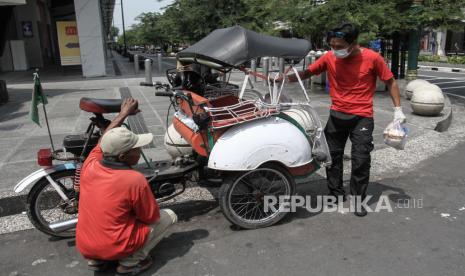 Relawan membagikan paket sembako kepada tukang becak di kawasan Malioboro, DI Yogyakarta, Jumat (27/3/2020). Pemberian bantuan sebagai jaring pengaman ekonomi bagi warga dengan pekerjaan mengandalkan pendapatan harian sebagai tukang becak, kusir andong dan pedagang kaki lima kawasan Malioboro seiring terus dilakukannya physical distancing untuk mencegah penyebaran COVID-19