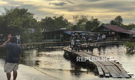 Sejumlah pengendara motor melintas di atas jembatan darurat di jalan utama Sintang-Putussibau yang terendam banjir di Kabupaten Sintang, Kalimantan Barat, Sabtu (13/11/2021). Penduduk setempat membangun jembatan darurat tersebut untuk membantu pejalan kaki, pengendara motor dan pesepeda yang melintasi jalan yang terendam banjir. 