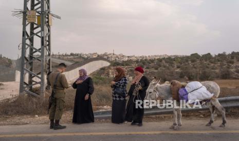 Seorang tentara Israel memeriksa izin masuk bagi petani Palestina untuk memungkinkan mereka menyeberang ke tanah mereka untuk memanen zaitun, di desa Beit Awwa, Tepi Barat, dekat Hebron, Rabu, 26 Oktober 2022. Tentara Israel untuk sementara membuka gerbang keamanan yang memisahkan beberapa petani Palestina di Tepi Barat dari kebun zaitun mereka di sisi pembatas pemisah Israel.