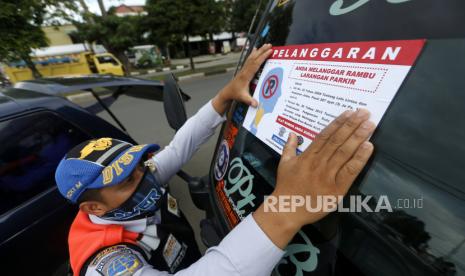 Petugas Dinas Perhubungan menempel striker pada mobil yang telah digembok karena parkir sembarangan.