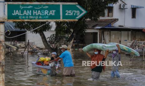 Seorang pria (kiri) mendorong troli dengan anak dan barang-barangnya, sementara anggota keluarga lainnya membawa kasur, setelah banjir melanda Taman Sri Muda, distrik Shah Alam, sekitar 40 km dari Kuala Lumpur, Malaysia, 21 Desember 2021. Pakar lingkungan memprediksi hujan lebat dan banjir akan sering melanda Malaysia.