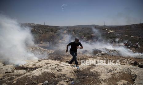 Seorang pengunjuk rasa Palestina berlari untuk berlindung dari tabung gas air mata yang ditembakkan oleh tentara Israel selama protes terhadap pos terdepan pemukiman Yahudi Tepi Barat Eviatar yang dengan cepat didirikan bulan lalu, di desa Palestina Beita, dekat kota Nablus, Tepi Barat, Jumat. 25 Juni 2021. 