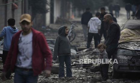 Seorang ayah Palestina dan anak-anaknya berdiri di tengah reruntuhan rumah mereka yang hancur akibat serangan udara Israel di Jalur Gaza selatan, 25 Desember 2023. 