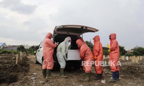 Pekerja yang mengenakan jas hazmat menurunkan peti mati berisi jenazah korban COVID-19 saat pemakaman di pemakaman Srengseng Sawah di Jakarta, 26 Maret 2021. 