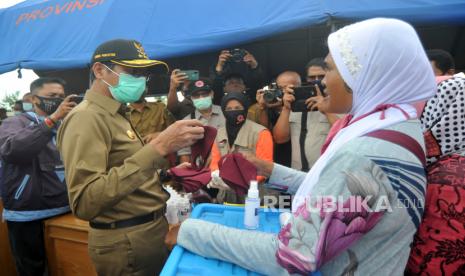 Gubernur Sumbar Irwan Prayitno (kiri) memberikan masker kepada pedagang yang tidak memakainya, saat sosialisasi di Pantai Cimpago, Padang, Sumatera Barat, Senin (14/9/2020). Pemprov Sumbar bersama pihak terkait hingga sepekan ke depan mensosialisasikan Perda Adaptasi Kebiasaan Baru yang memiliki sanksi administratif dan pidana jika tidak menggunakan masker, sekaligus membagikan secara gratis 18.000 helai masker dan 8.000 botol handsanitizer kepada masyarakat. 