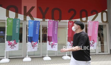 Seorang pria yang mengenakan masker untuk melindungi diri dari penyebaran virus corona berjalan dengan mengibarkan bendera untuk mempromosikan Olimpiade di Tokyo, Senin, 26 Juli 2021.