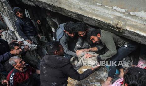 Warga Palestina menyelamatkan anak laki-laki yang terluka di antara puing rumah yang hancur akibat serangan udara Israel di kota Deir Al Balah, Jalur Gaza selatan, (18/2/2024).