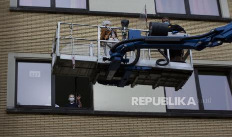 Bernadette Focant (kiri) dari jendela lantai tiga saat ia menerima kunjungan saudara perempuannya dengan crane di Watermael-Boitsfort, Belgia, Sabtu (9/5). Tristan Van den Bosch, seorang operator crane, melihat peralatan crane menganggur karena pandemi virus corona dan banyak keluarga yang tidak dapat melihat lansia yang terkunci di rumah perawatan