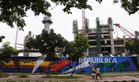 Warga melintas di depan proyek pembangunan Jakarta International Stadium atau Stadion Bersih, Manusiawi, dan Wibawa (BMW) di kawasan Papanggo, Tanjung Priok, Jakarta, Ahad (17/1/2021). Progres pembangunan stadion berkapasitas 82 ribu penonton tersebut telah mencapai 43,7 persen dan ditargetkan rampung pada Oktober 2021.