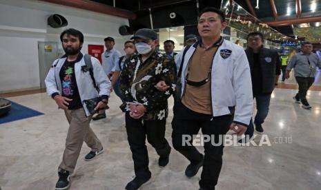  Petugas Dittipidsiber Bareskrim Polri membawa  peneliti dari Badan Riset dan Inovasi Nasional (BRIN) Andi Pangerang Hasanuddin (tengah) setibanya di Terminal 2 Bandara Soekarno, Hatta, Tangerang, Banten, Ahad (30/4/2023). Andi Pangerang Hasanuddin ditangkap terkait komentarnya yang bernada ancaman terhadap warga Muhammadiyah beberapa waktu lalu di media sosial.  