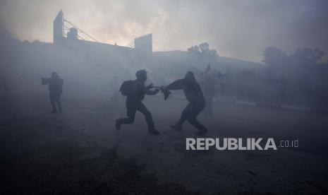 Seorang pengunjuk rasa Palestina dan seorang tentara Israel menarik bendera Palestina di tengah asap dari bom suara, selama demonstrasi setelah pemukim Yahudi mencoba untuk memblokir anak-anak Palestina memasuki sekolah di desa al-Lubban al-Sharqiya, dekat kota Tepi Barat. Nablus, Minggu, 27 Februari 2022. 