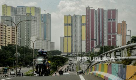 Pengendara motor melintas dengan latar belakang Wisma Atlet Kemayoran yang difungsikan sebagai Rumah Sakit Darurat COVID-19 di Jakarta, Selasa (14/4). 