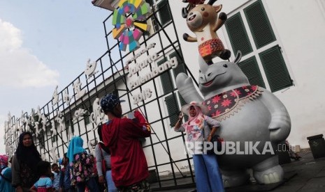 Sejumlah wisatawan berfoto dengan patung maskot Asian games di Kota Tua, Jakarta, Ahad (17/6).