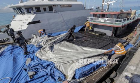 Personel TNI AL mengawasi tersangka ABK membuka terpal penutup ribuan rokok ilegal yang diselundupkan di Dermaga Pangkalan TNI AL (Lanal) Batam, Kepulauan Riau, Ahad (28/3/2021). Patroli keamanan laut TNI Angkatan Laut KRI Alamang-644 berhasil mengamankan kapal beserta delapan orang ABK yang menyelundupkan rokok ilegal sebanyak 1673 karton berbagai jenis rokok dari Jurong, Singapura. 