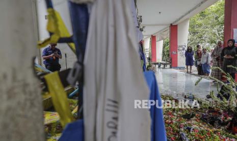 Seorang petugas polisi forensik menyelidiki di dekat pintu masuk tribun 13, lokasi utama penyerbuan, saat kerabat menyampaikan belasungkawa kepada para korban di Stadion Kanjuruhan di Malang, Jawa Timur, Indonesia, 06 Oktober 2022. Presiden Indonesia telah memerintahkan penyelidikan dan audit ke seluruh stadion sepak bola di tanah air, untuk memastikan keamanan bagi para penggemar setelah setidaknya 131 orang tewas dalam kerusuhan dan penyerbuan menyusul pertandingan sepak bola antara Arema FC dan Persebaya Surabaya di Jawa Timur pada 01 Oktober 2022.