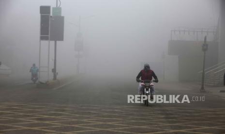 Seorang pengendara sepeda motor melaju di jalan raya saat kabut tebal mengurangi jarak pandang di Peshawar, Pakistan, Selasa, (23/1/2024).