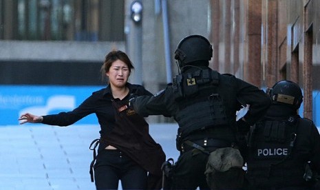  Sejumlah polisi bersenjata lengkap mengamankan seorang wanita yang berhasil melarikan diri dari penyanderaan di sebuah kafe di Sydney, Senin (15/12). (AP/Rob Griffith)